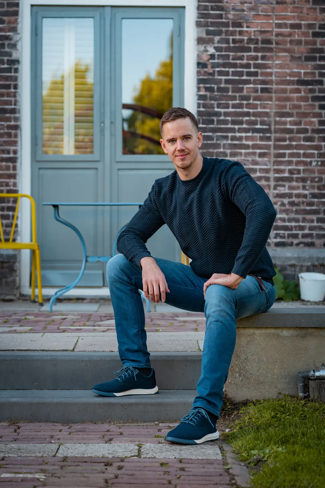 Jochem Brem zit op een stoep voor een bakstenen gevel en kijkt in de camera